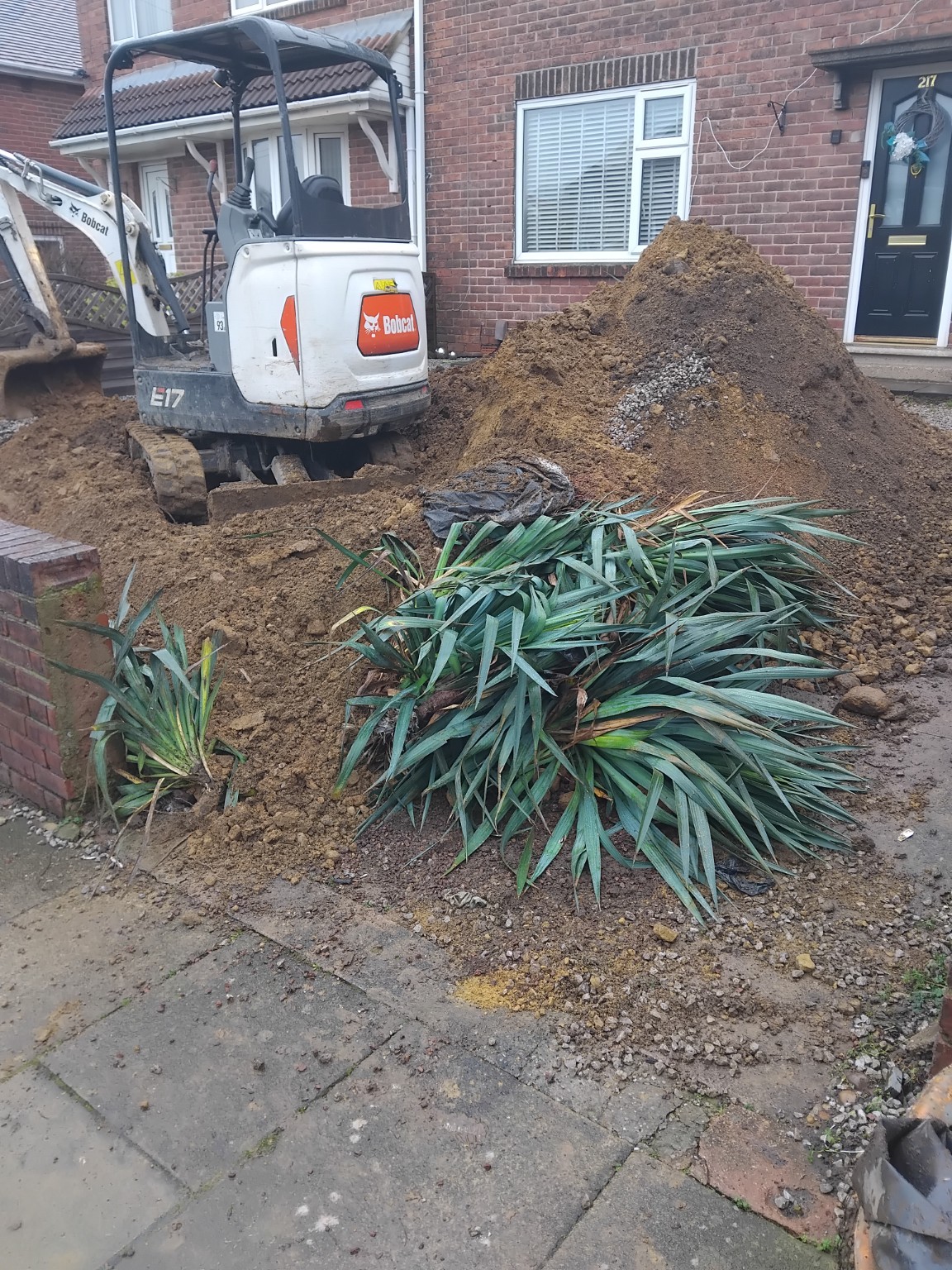 Mini excavator clearing a front garden with excavated soil and removed plants