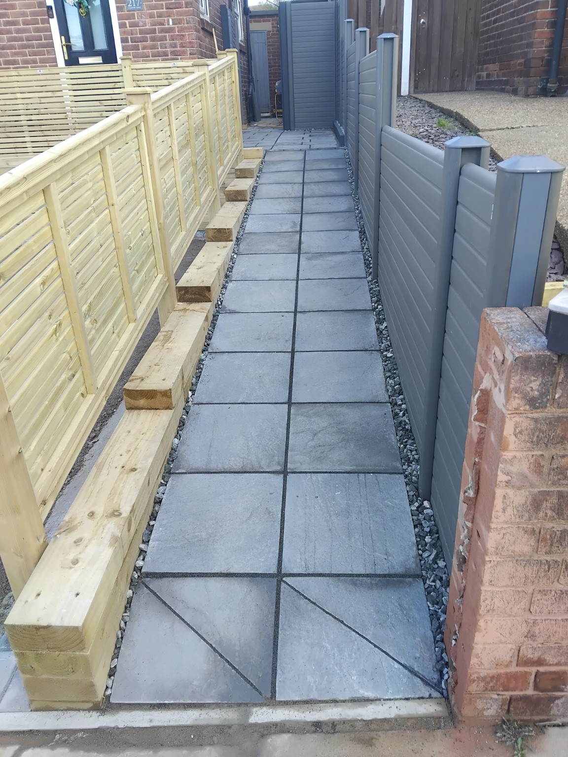 Completed grey paved access path between timber screening and grey fencing