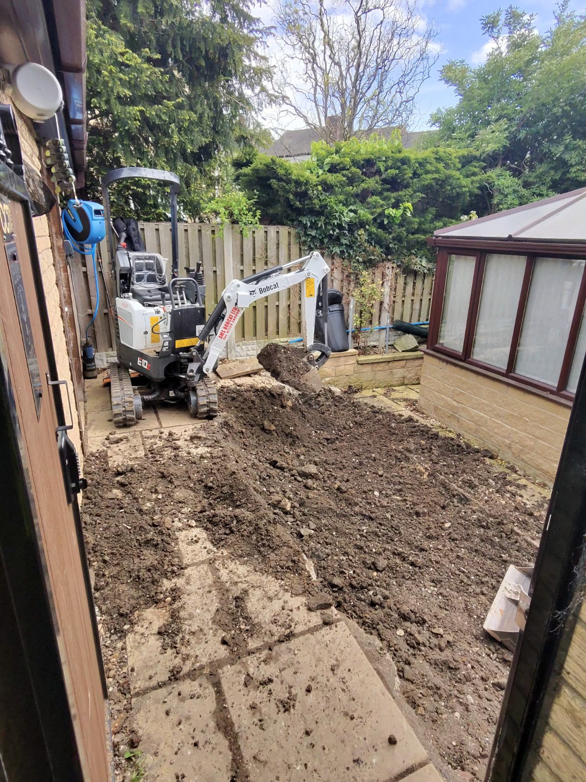 Compact excavator removing ground beside a house and conservatory for an extension