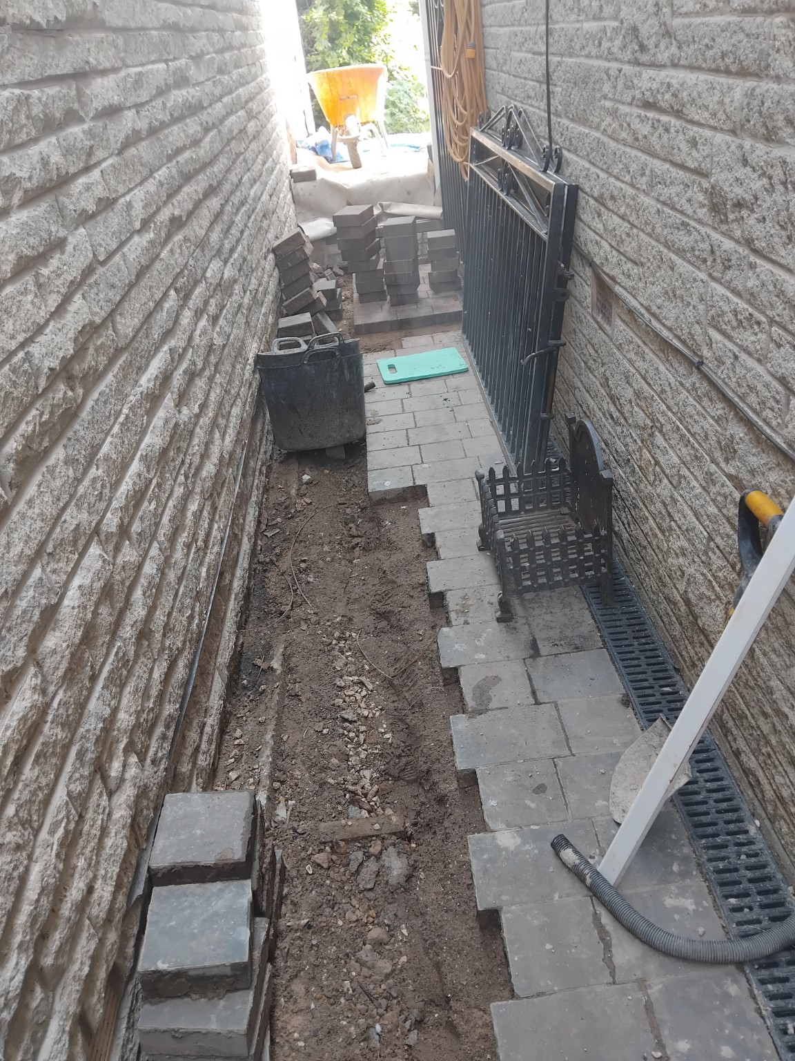 Partly laid block paving in a narrow side passage beside channel drainage