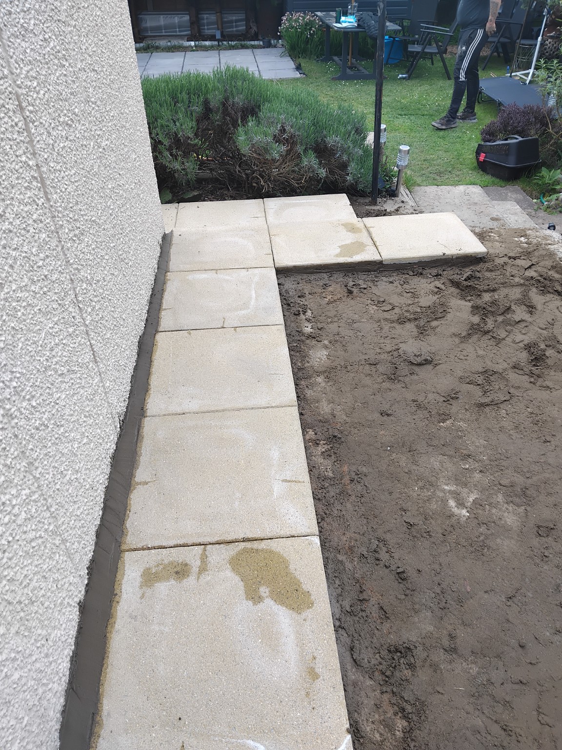 Pale paving slabs being laid beside the rendered wall of a house
