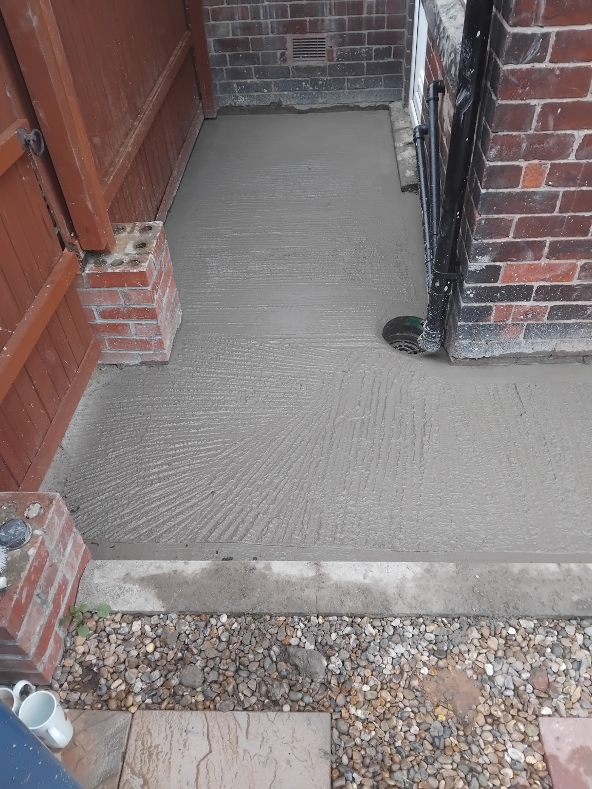 Freshly laid textured concrete path around a rainwater gully