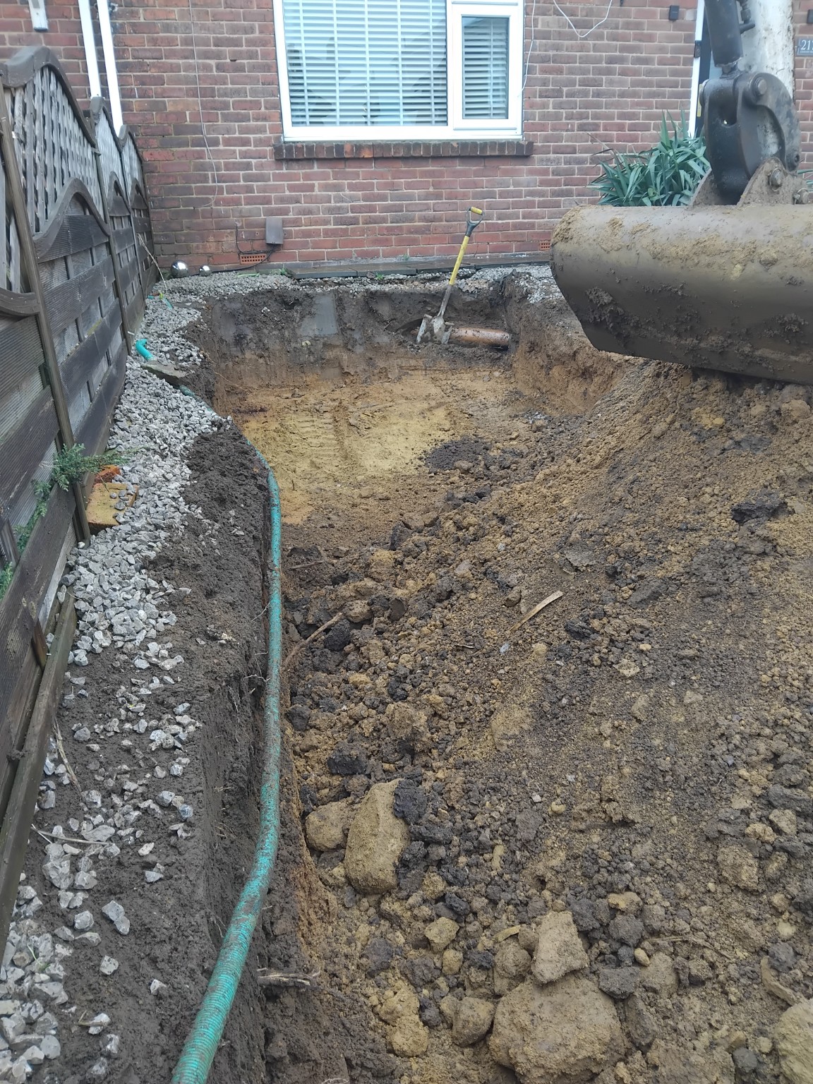 Excavated front garden with exposed ground and a mini excavator bucket