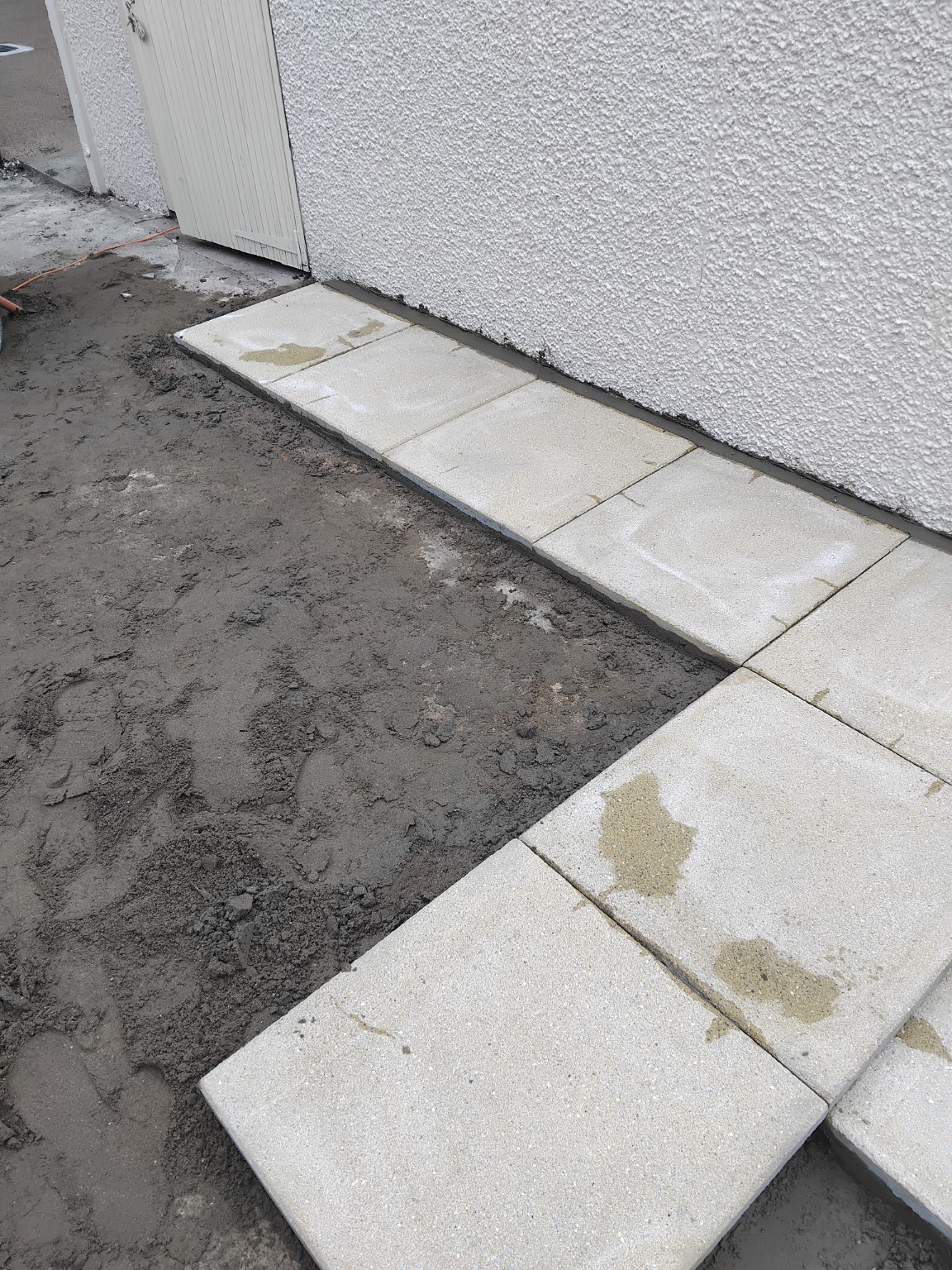 First rows of paving slabs set around the edge of the prepared patio area