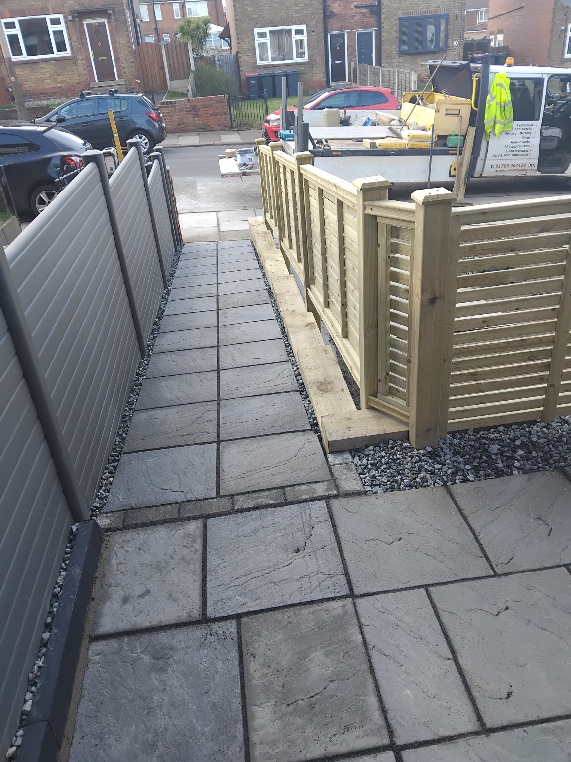 Paved entrance path alongside timber sleeper walls and grey fencing