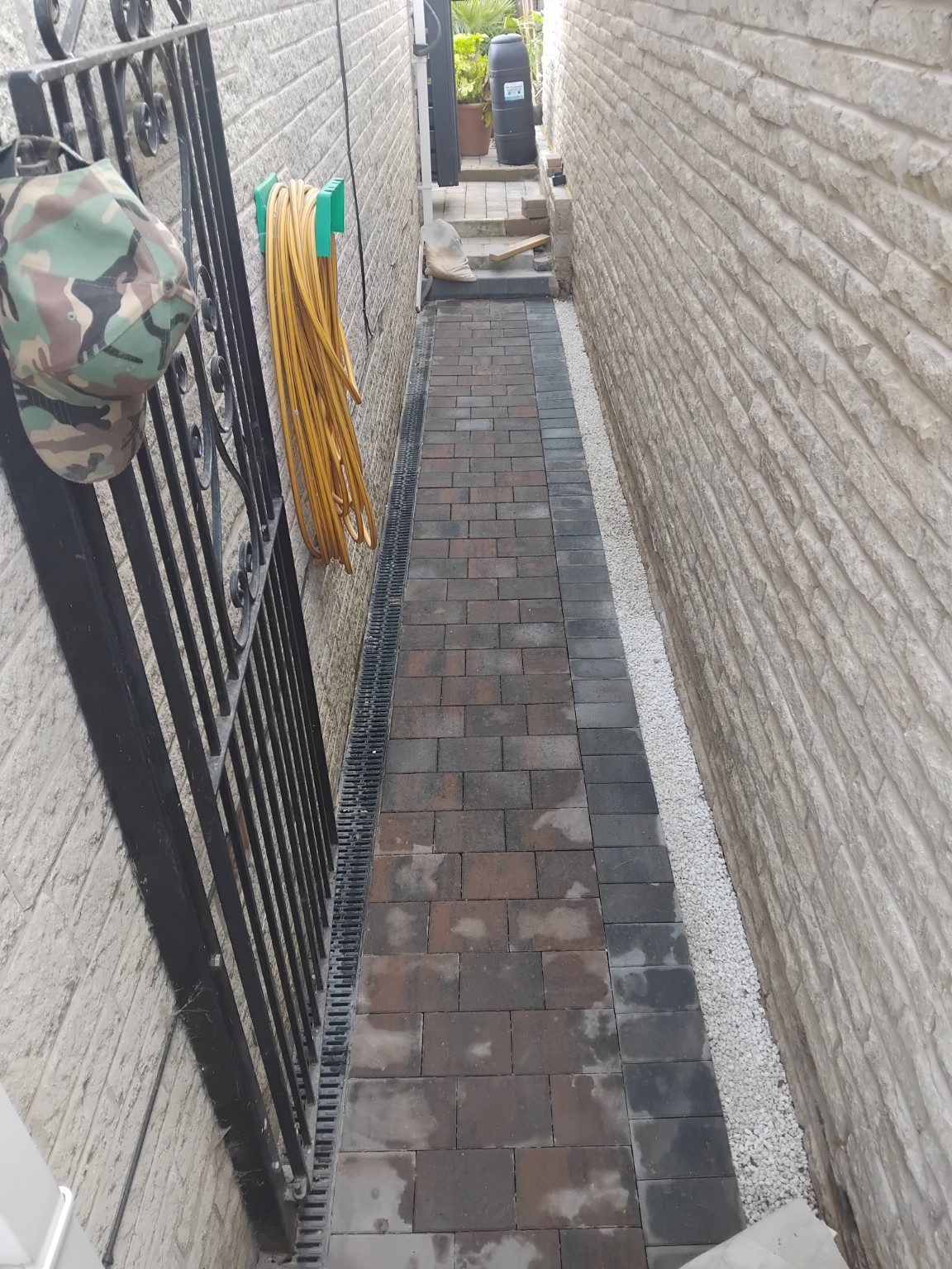 Completed block paved side path between stone walls with drainage and a gravel border