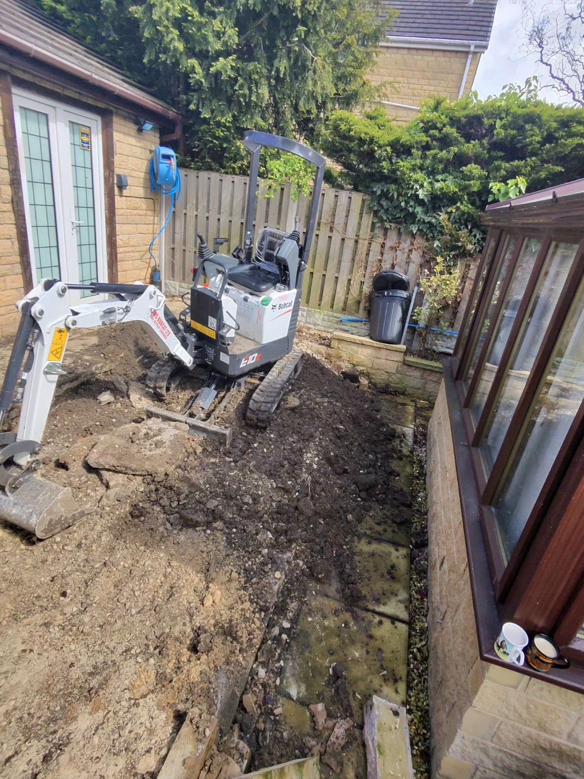 Compact excavator working in the space between a house and conservatory