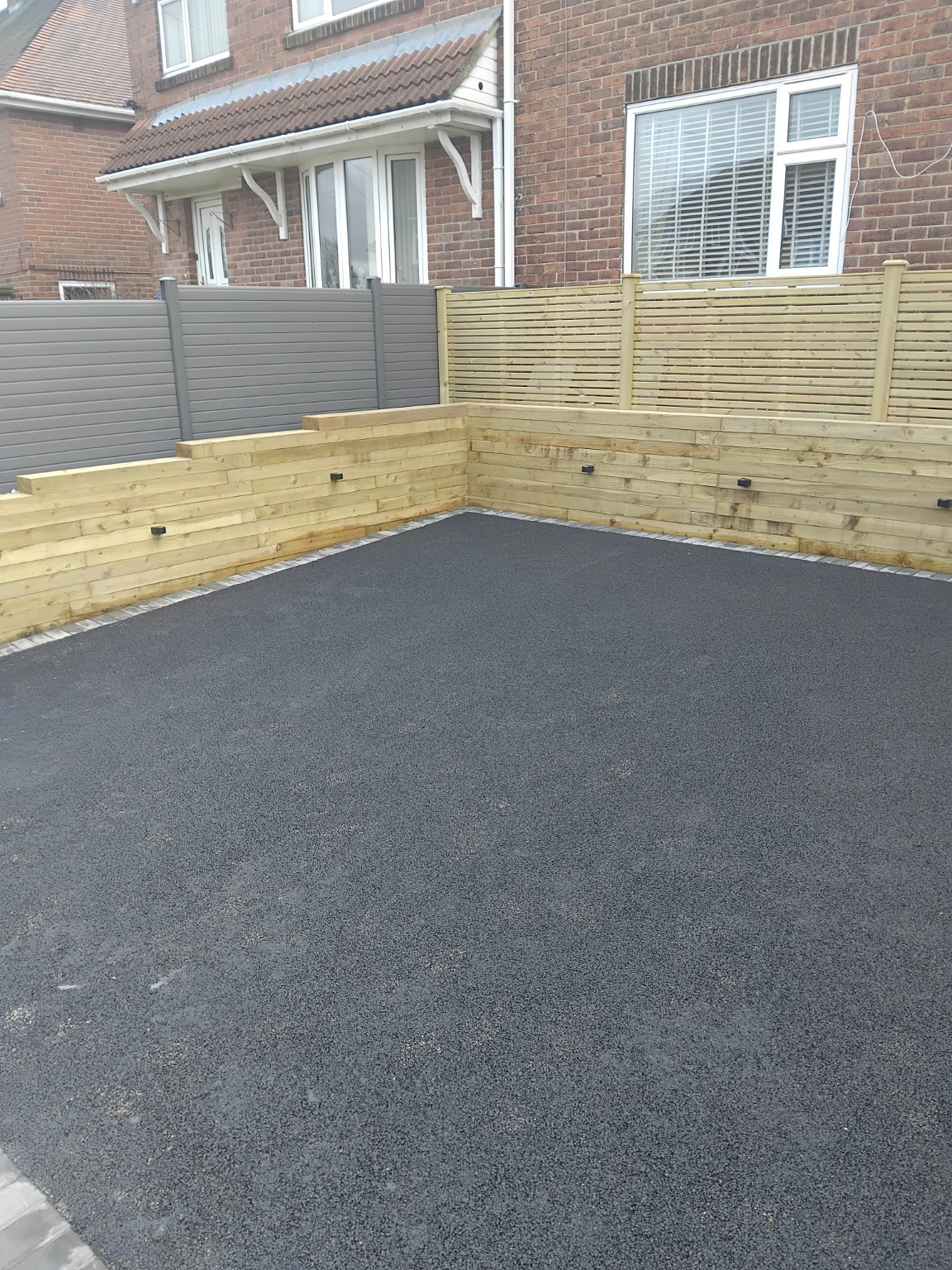 New dark driveway surface bordered by timber sleeper retaining walls