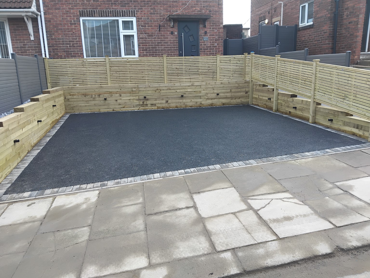 Wide view of the completed dark driveway with block edging and timber screening