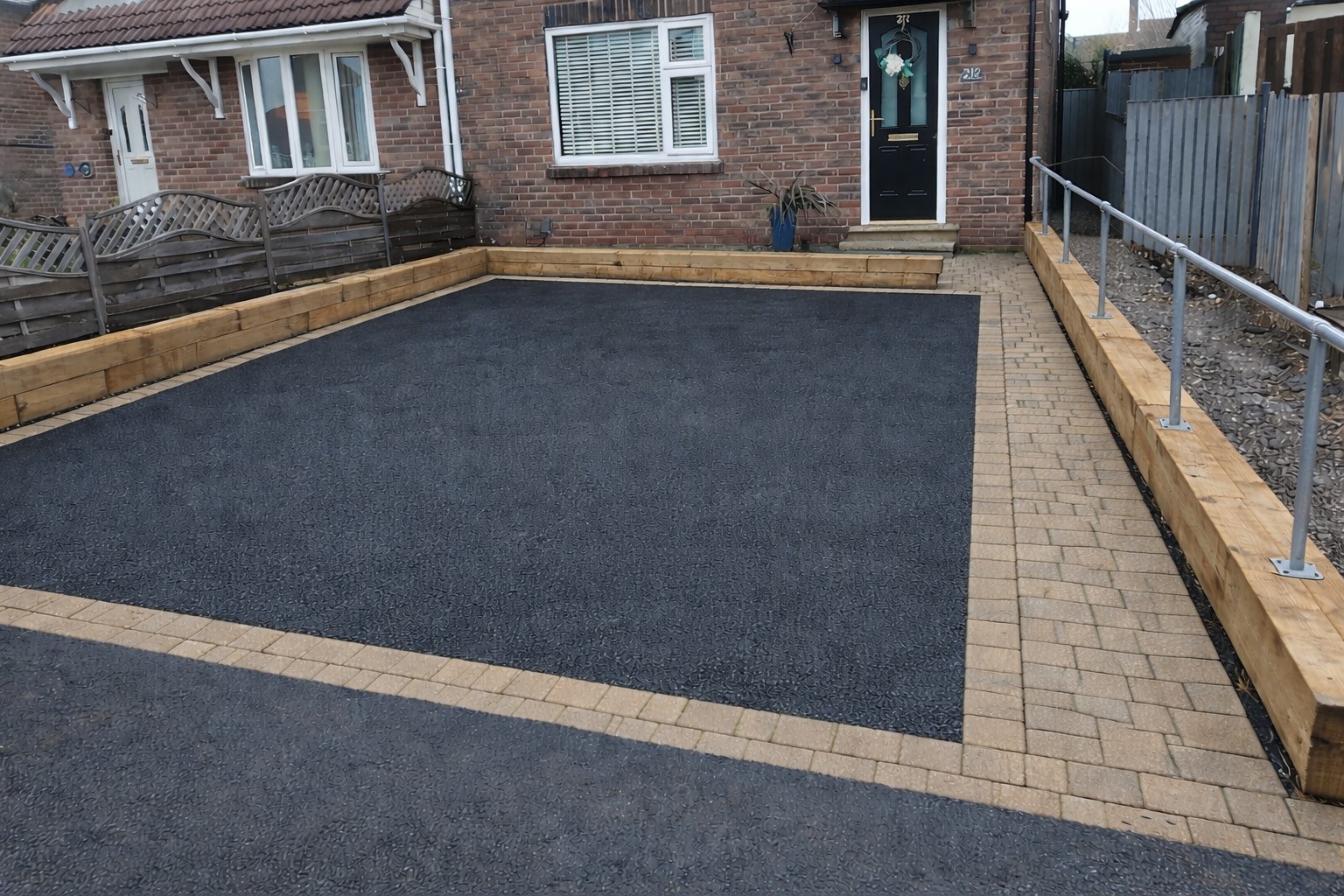 After: finished driveway with a dark surface, contrasting block borders and new fencing