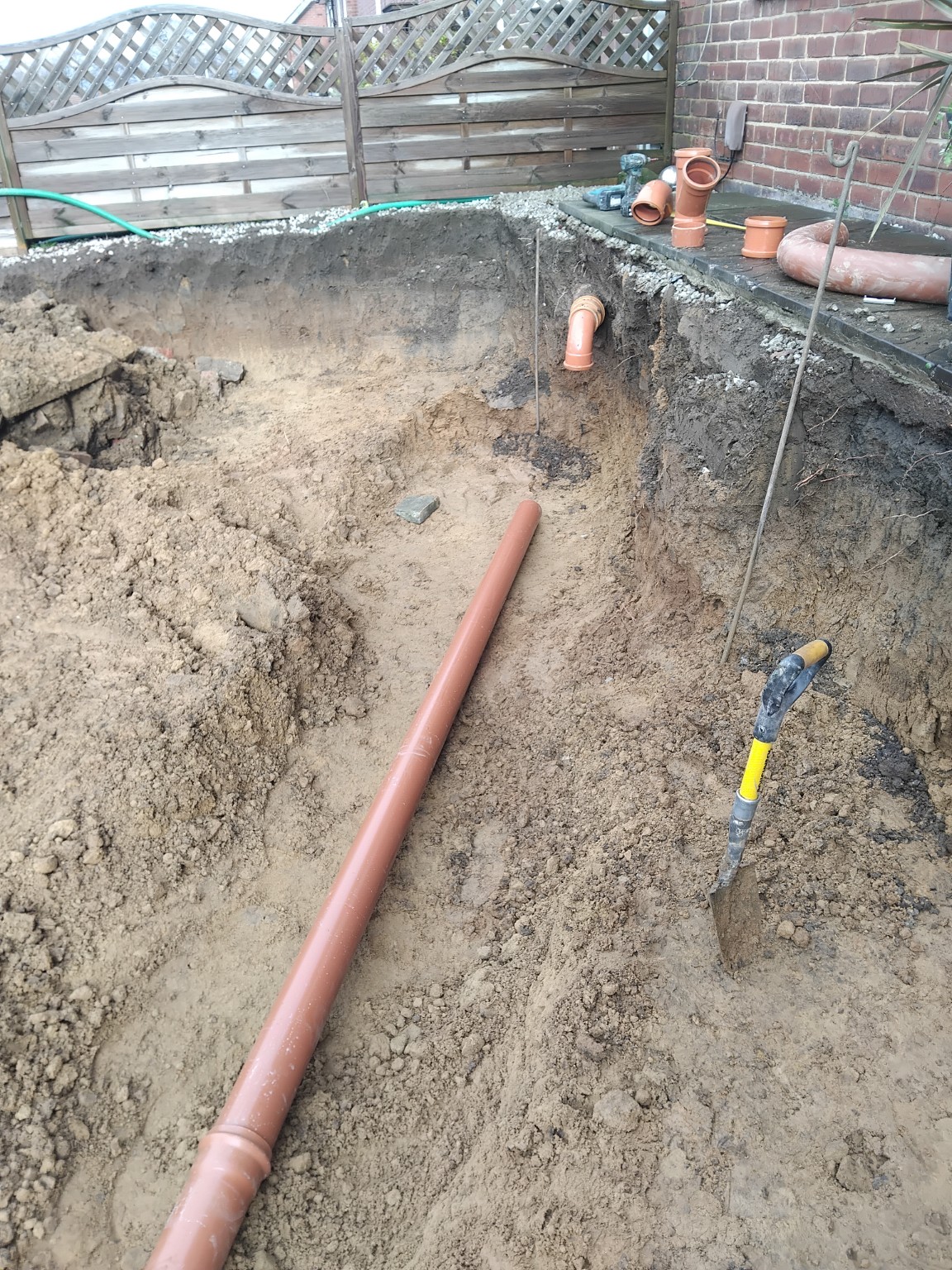 Drainage pipework in an excavated trench beside a brick wall
