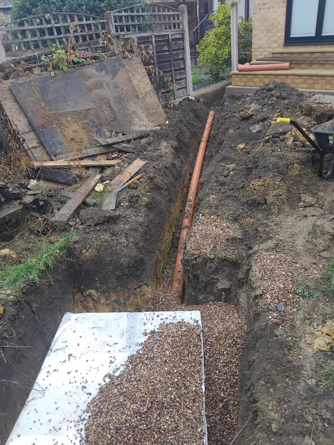 Excavated trench and drainage pipe beside a residential property