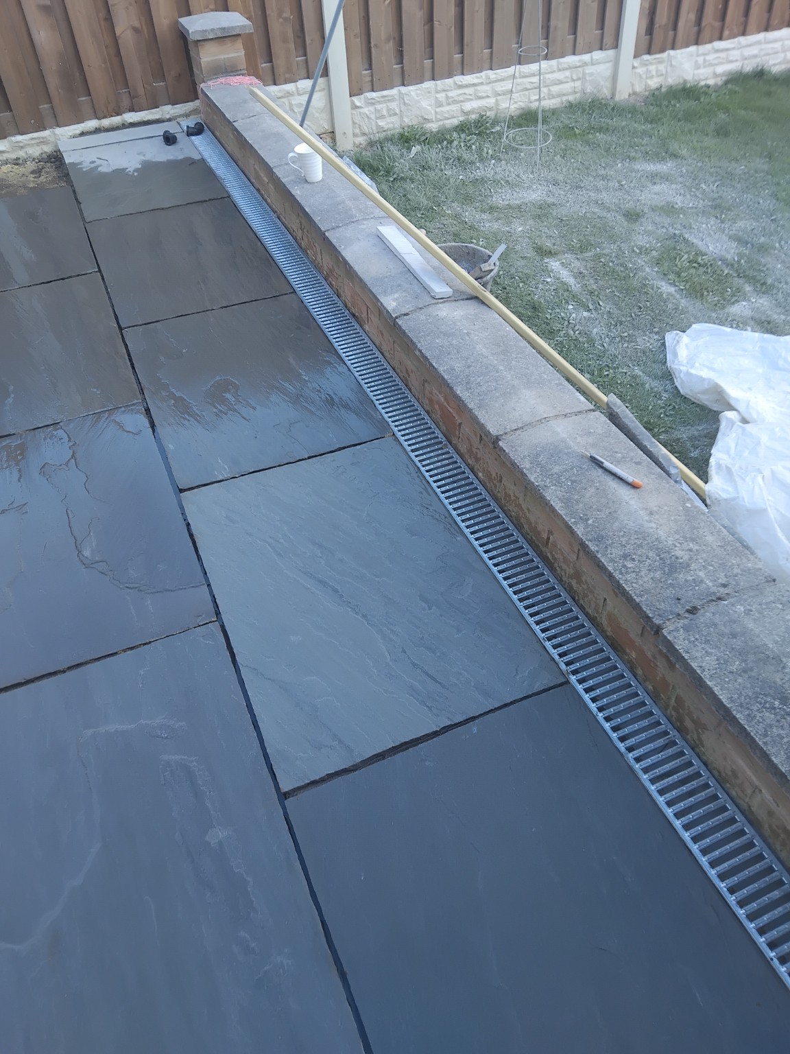 Grey paving beside a brick garden wall with a linear drainage channel