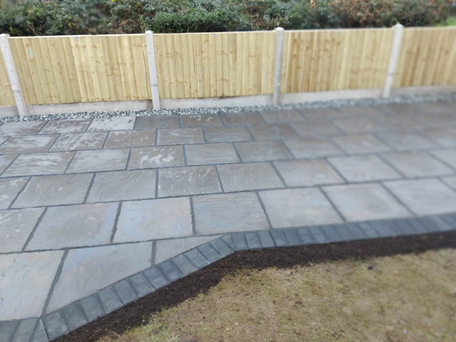 Finished grey paved patio with a dark block border and timber fencing